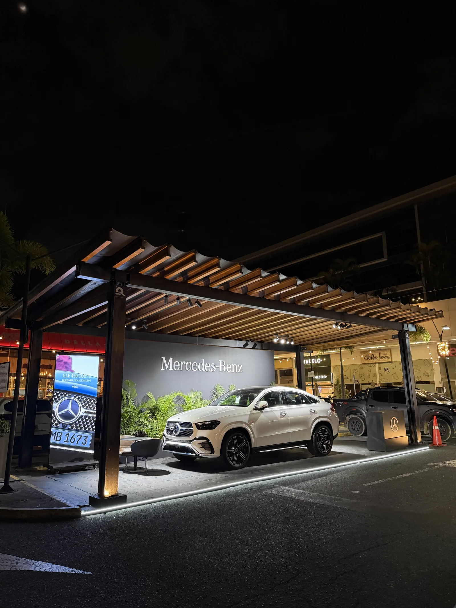 Carro de Mercedes-Benz en exhibición bajo pérgola de madera, de noche