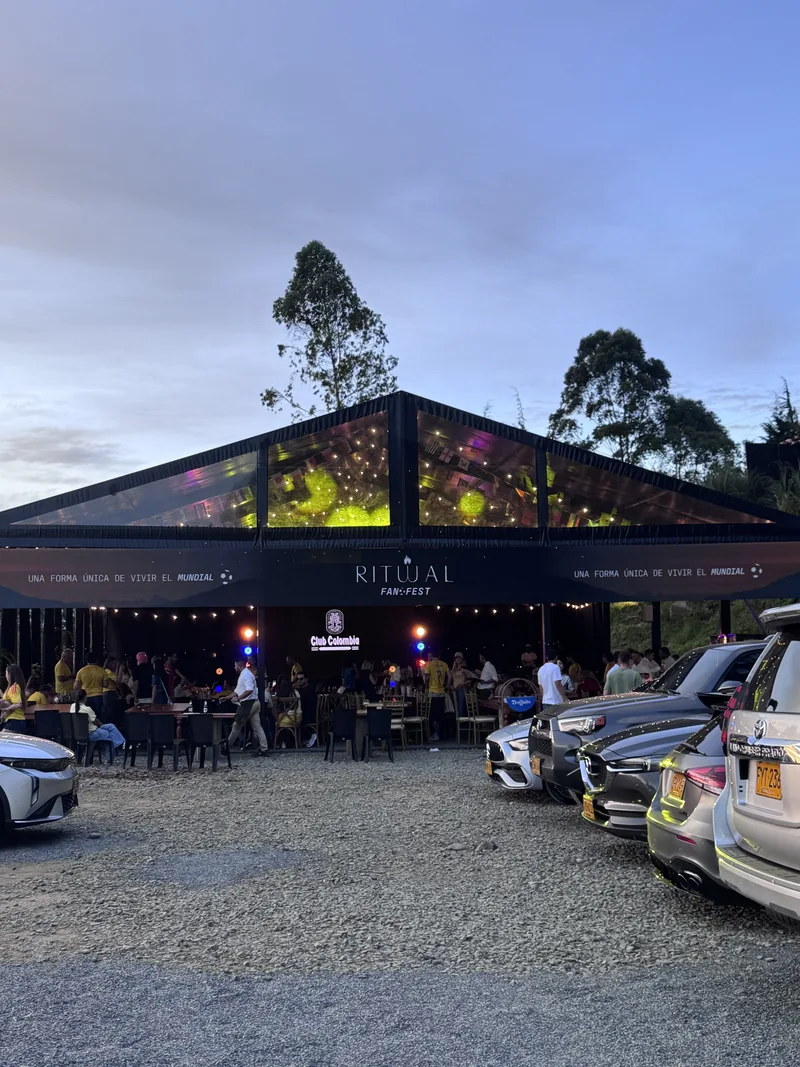 Pabellón de techo translúcido iluminado de noche, con público y carros en la entrada
