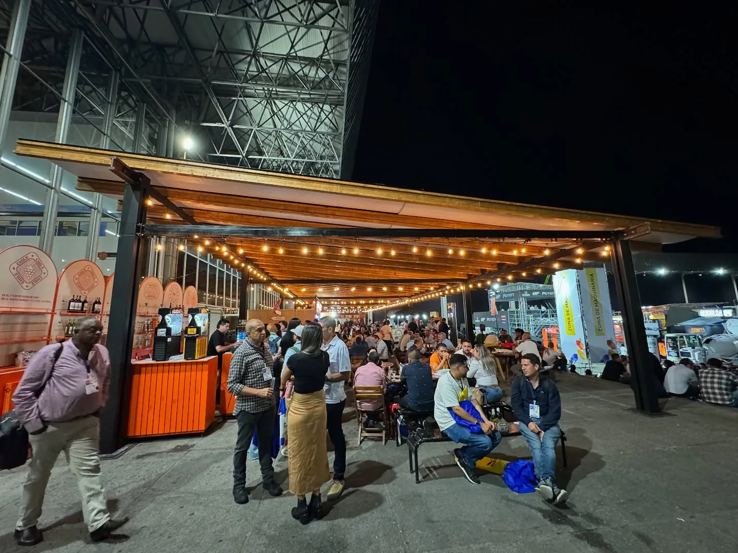 Público de feria bajo pérgola de madera con guirnaldas de luz