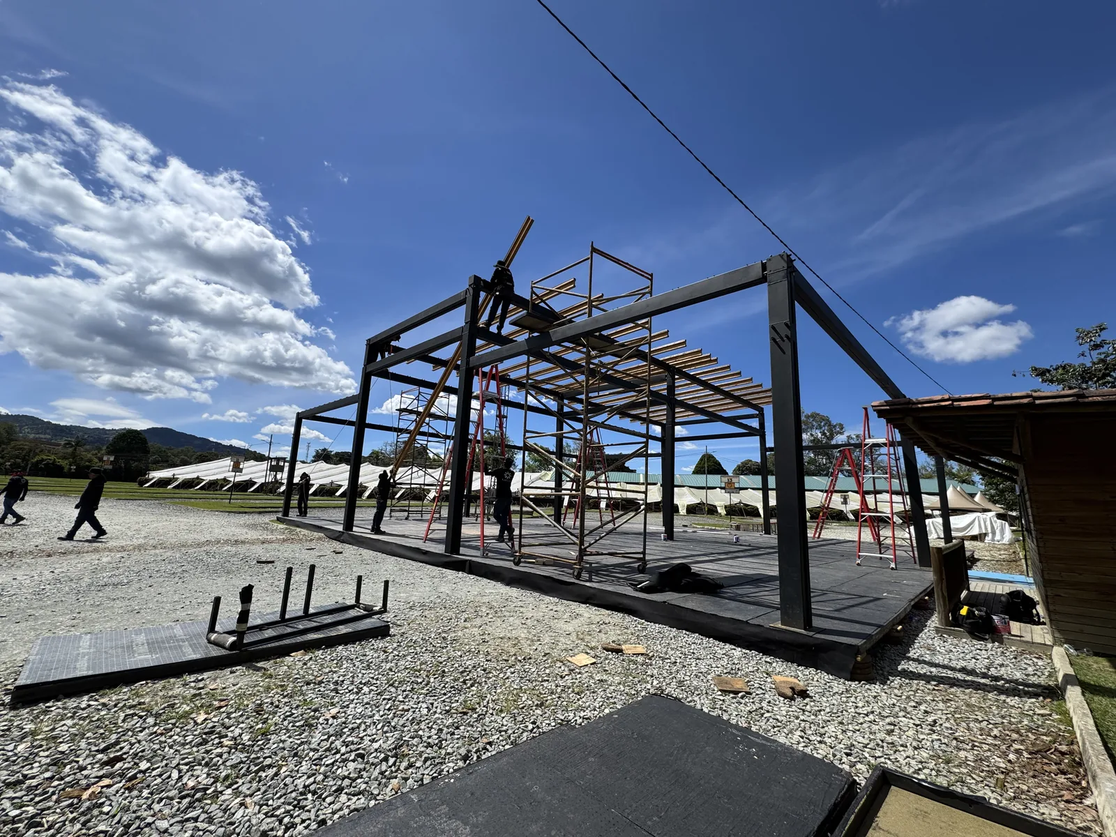 Esqueleto de acero de una pérgola en montaje sobre la tarima, con cielo azul en Llanogrande