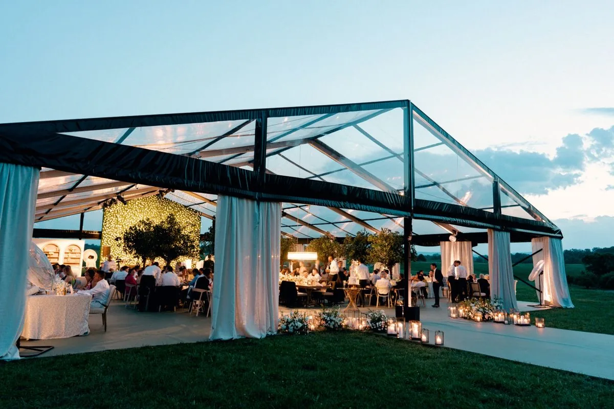 Pabellón de techo transparente con cortinas y cena de boda al atardecer
