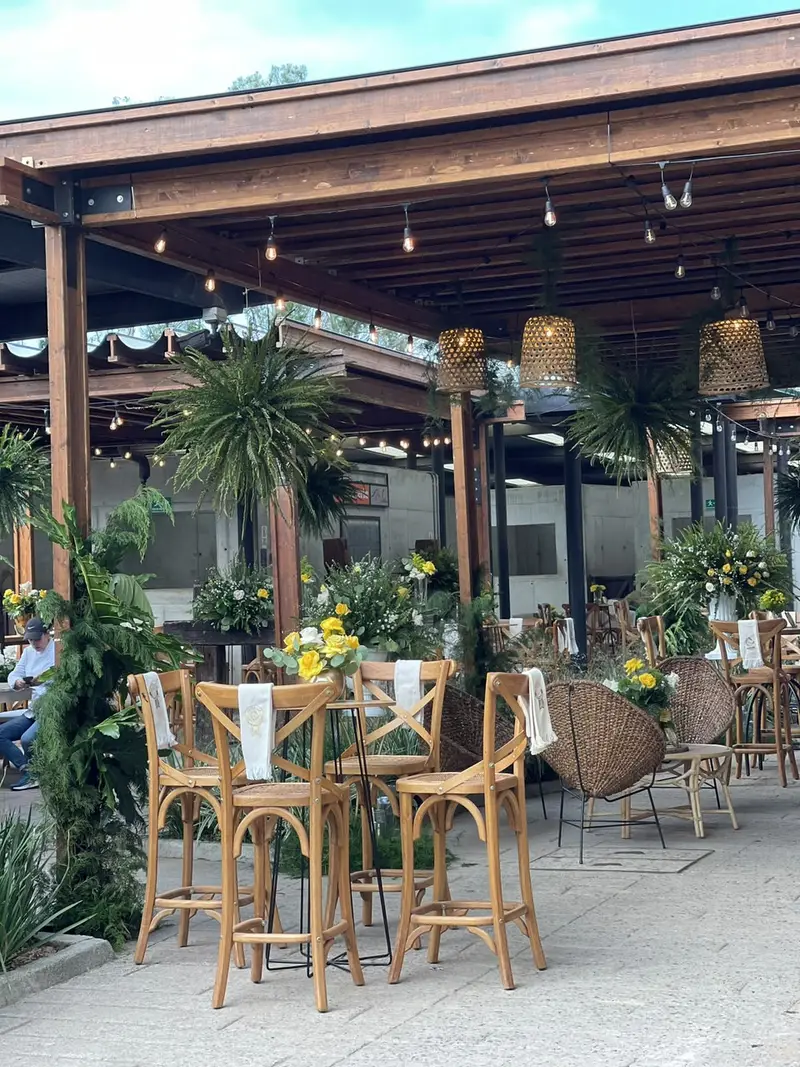 Mesas altas y flores bajo pérgola de madera con lámparas de mimbre
